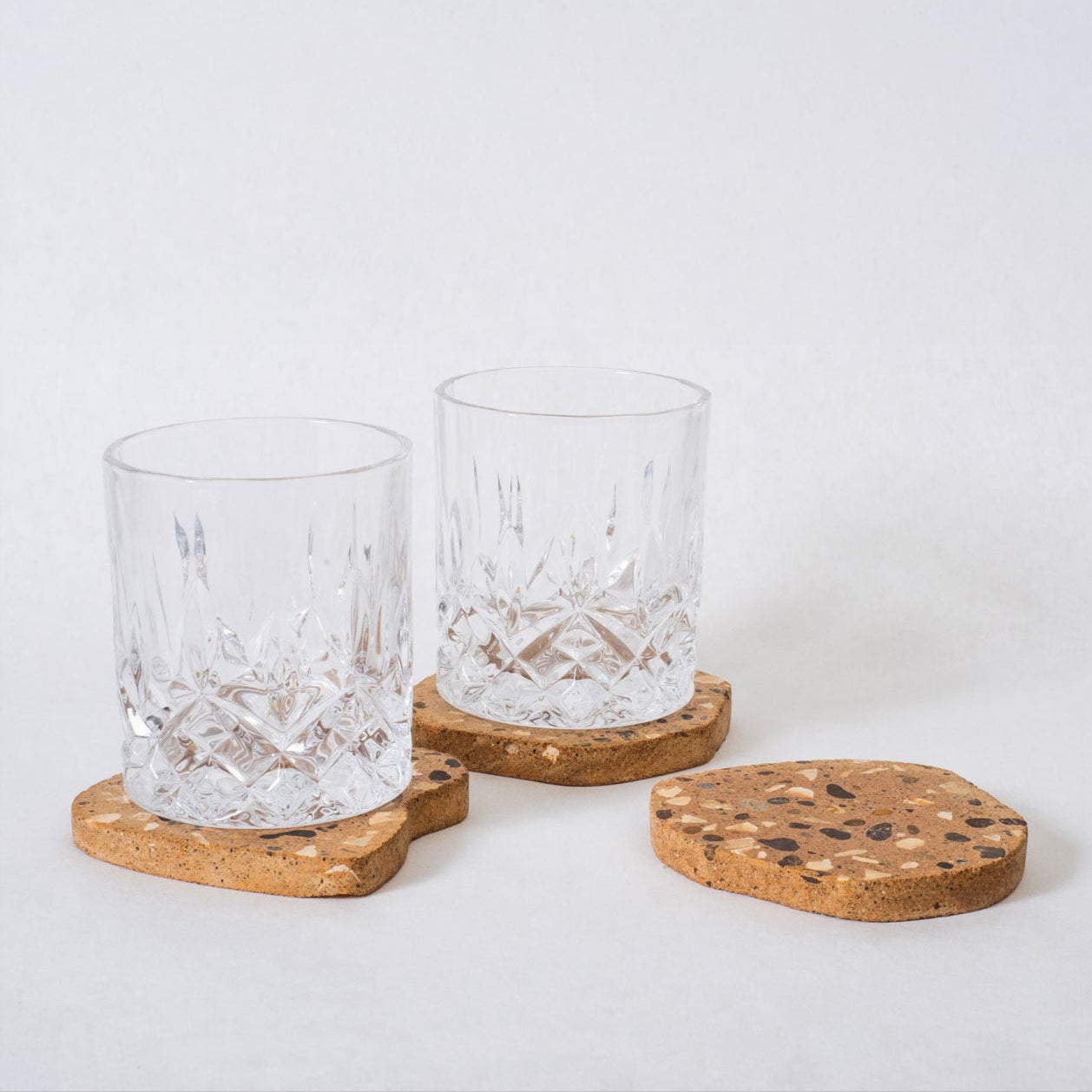Two clear glasses with wooden coasters on a white background