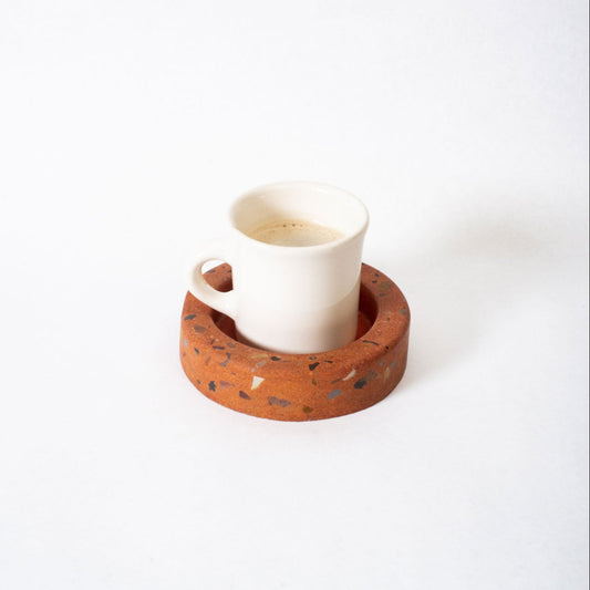 White ceramic cup with a terracotta-colored coaster on a white background