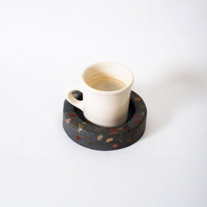 White ceramic cup on a black terrazzo coaster with a white background