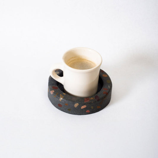 White ceramic cup on a black terrazzo coaster with a white background